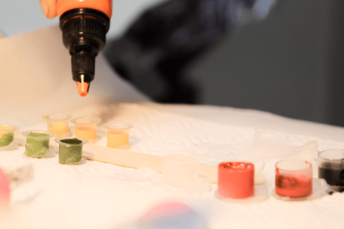 Tatuador preenchendo batoques com tinta colorida sobre bancada preparada.