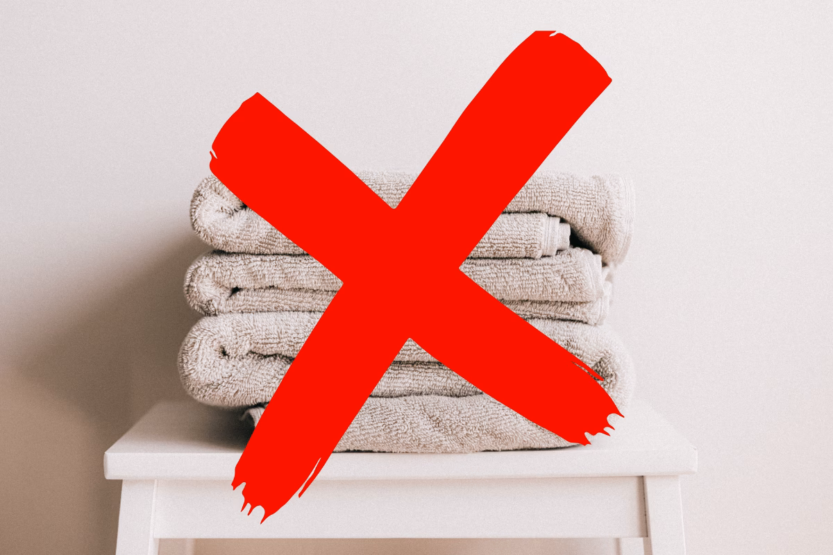 Imagem de toalhas de banho com um X vermelho, indicando que é errado secar a tatuagem nova com elas devido ao risco de bactérias e contaminação, devendo-se usar papel toalha.